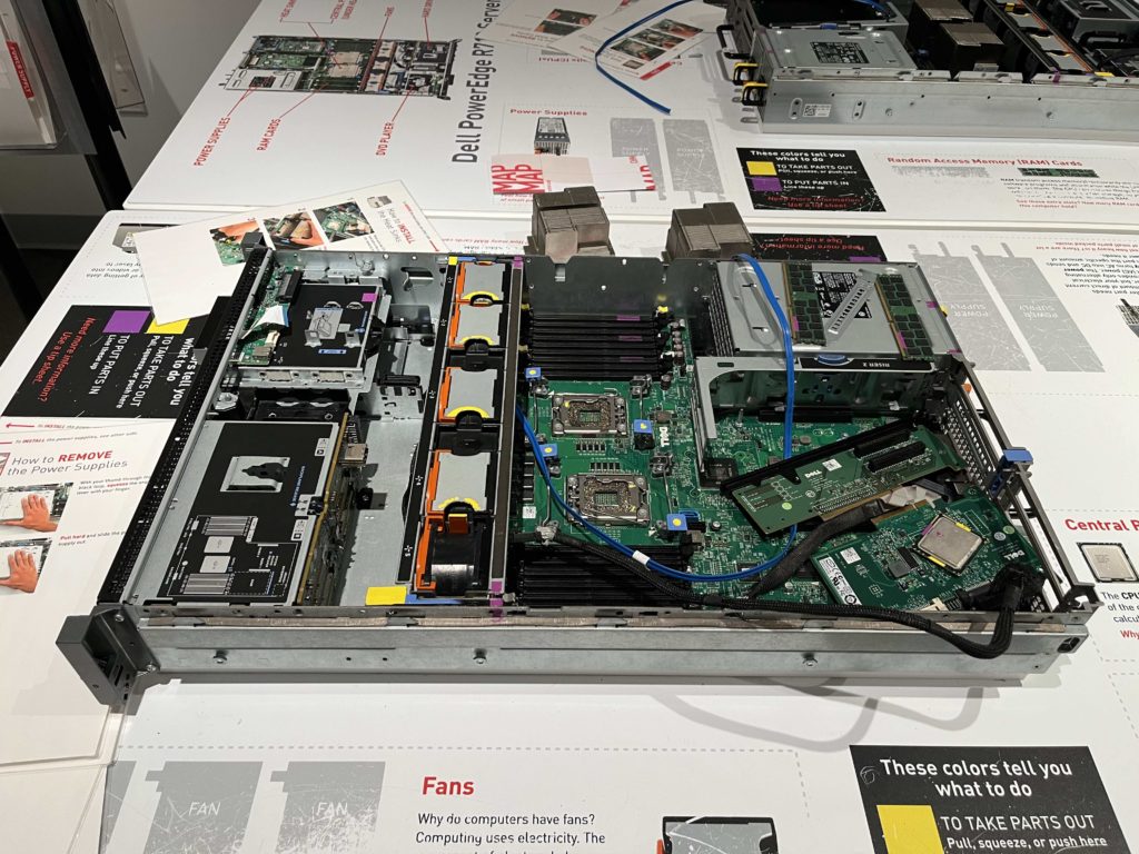 A Dell PowerEdge R710 lays on a white plastic table, top cover off, surrounded by instructions on how to disassemble it.